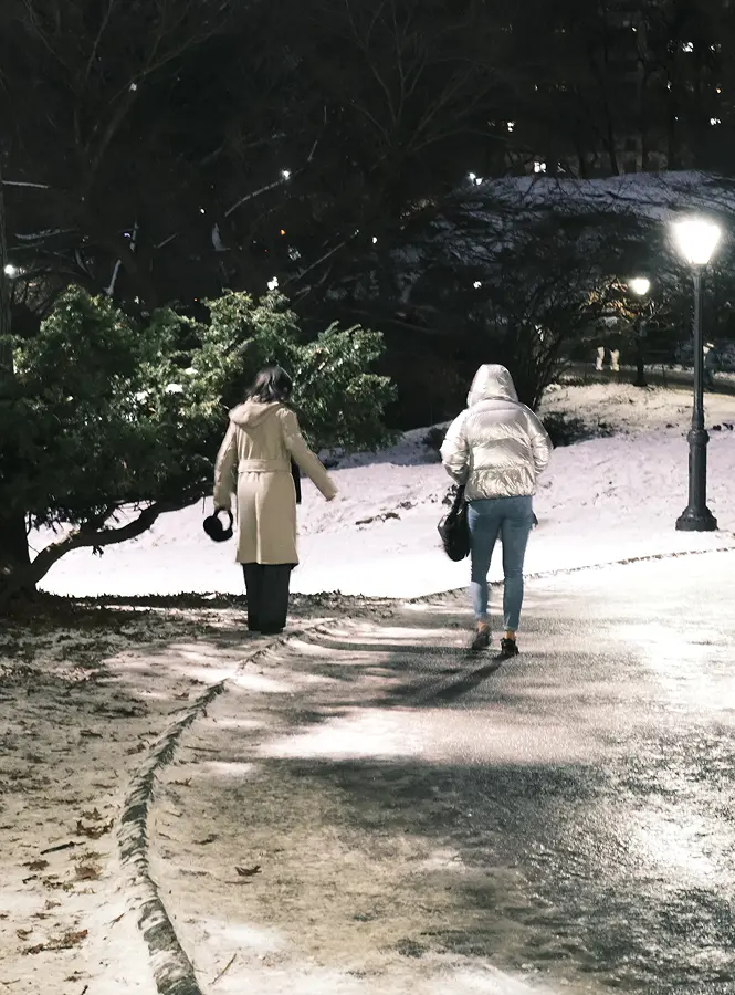 Two people walking through a snowy park at night